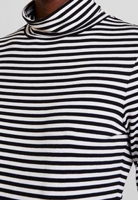 Svart- och vitrandig polokrage-tröja med en figursydd design och mjukt material. Ränderna varierar i bredd, vilket framhäver stilen.