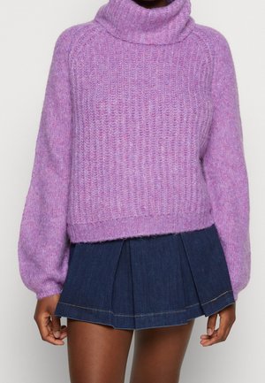 Femme portant un pull à col roulé en tricot violet à manches longues et une mini-jupe plissée bleu foncé.