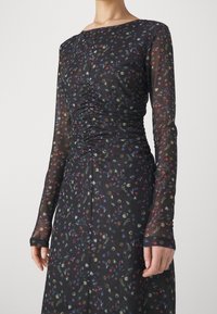 Mustapohjaista pitkähihasta mekkoa, jossa on kukkakuosi, ja joka sisältää keräilytietoa vartalon kohdalla ja tiukasti istuvat hihat, valmistettu läpikuultavasta kankaasta.