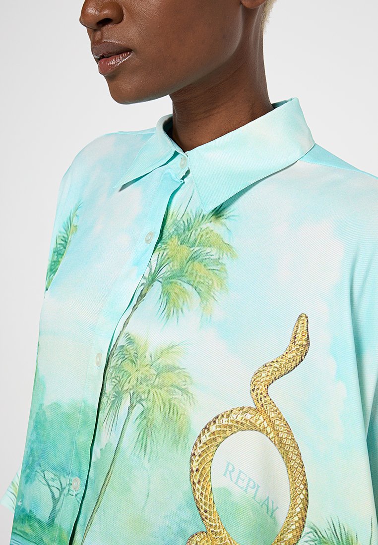 Jasnoniebieska koszula z krótkim rękawem i kołnierzykiem zapinanym na guziki, z nadrukiem palm i złotym wężem oraz napisem "REPLAY". Gładka tekstura.