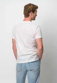 T-shirt bianco in cotone con maniche corte e scollatura rotonda, abbinato a jeans in denim azzurro chiaro. La vista posteriore mostra una trama liscia.