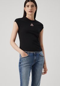 Svart tettsittende T-skjorte med korte ermer og rund hals, med en rosa "DIESEL"-logo på forsiden. Brukt sammen med blå denimjeans.