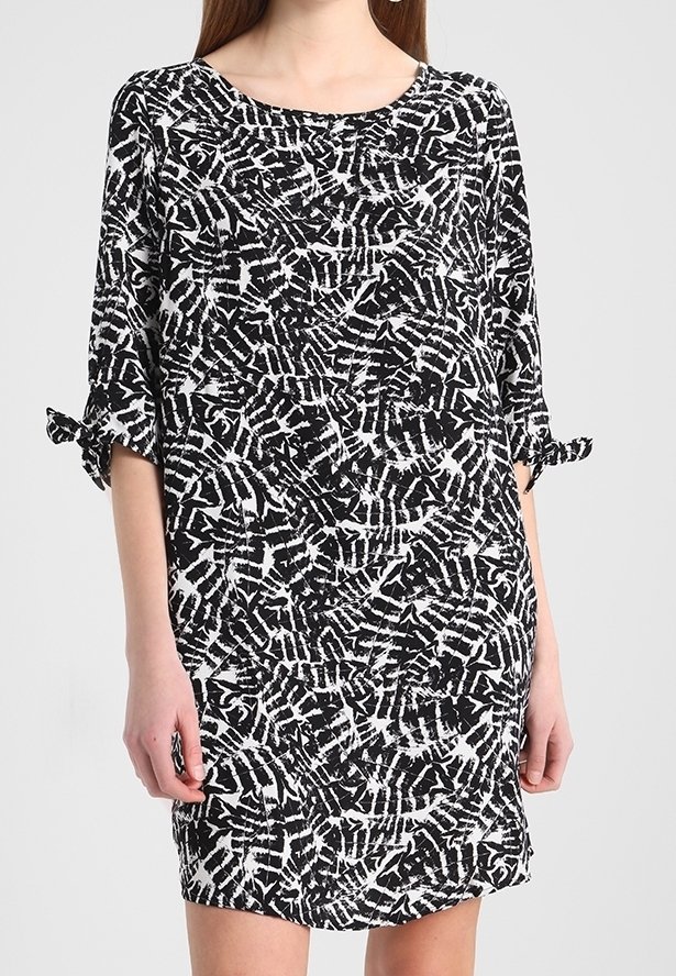 Femme portant une robe à motifs noir et blanc jusqu'aux genoux avec des manches au coude nouées en nœuds aux poignets.