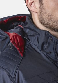 Marineblau gesteppte Jacke mit rotem Futter, verfügt über einen hohen Kragen, Knopf- und Reißverschluss sowie ein strukturiertes Gewebe.