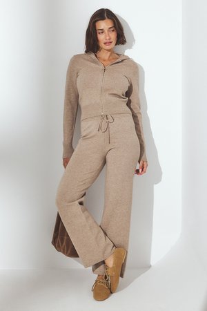 Chándal de punto beige con sudadera con cremallera, cintura ajustable con cordón, pantalones de pierna ancha y textura suave. Combinado con zapatos de ante marrón.