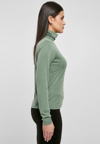 Pulover cu guler înalt, cu mânecă lungă, de culoare verde închis, realizat dintr-un material moale. Design mulat cu textură netedă, cu linii curate și fără modele vizibile.