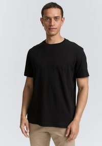 Sort kortærmet t-shirt i bomuldsstof med rund halsudskæring. Lige snit og minimalistisk design, båret over beige bukser.
