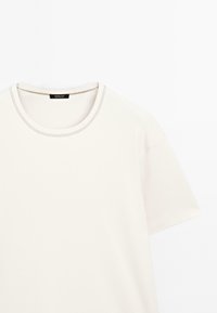 T-shirt a maniche corte, collo tondo, in off-white, realizzato in cotone. Presenta cuciture sottili lungo il collo e una vestibilità comoda.
