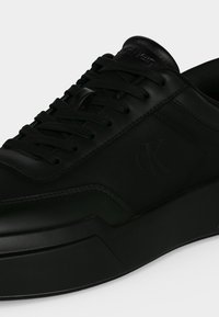 Baskets basses noires avec semelle épaisse, dessus en cuir lisse, lacets noirs et logo subtil "ck" sur le panneau latéral.