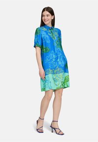 Abito camicia a maniche corte di colore blu con motivi paisley verdi; presenta un colletto, una silhouette ampia e un orlo sfumato che passa a un verde chiaro.