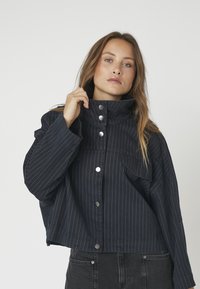 Marineblaues, kurzes Jackett mit vertikalen Streifen, hohem Kragen, Vorderblende mit silbernen Knöpfen und lässigem, oversized Schnitt.