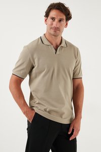 Beige polo särk, valmistatud tekstureeritud kangast, millel on kolme nupuga kaelus ja kontrastsed mustad aktsendid kaeluses ja varrukatel.