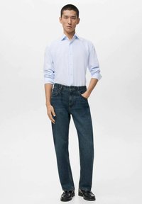 Camicia button-up a righe blu chiaro abbinata a jeans a gamba dritta blu scuro e scarpe nere. Vestibilità dritta, design minimale, senza motivi visibili.