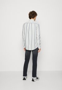 Gestreepte langemouwen shirt in wit en lichtblauw, gecombineerd met donkere spijkerbroek. Heeft een gebogen zoom en knoopmanchetten. Sneakers met zwarte accenten.