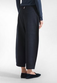 Donker, wijd-uitlopende broeken van zachte stof met een gestructureerd oppervlak. Voorzien van een contrasterende tailleband, zijzakken en gestyled met zwarte slippers.