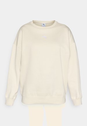 Felpa beige con collo rotondo classico, vestibilità ampia e polsini a coste. Presenta un piccolo logo Puma viola sul petto. Tessuto morbido.