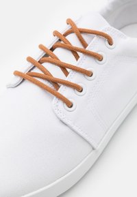 Baskets en toile blanches avec des lacets beige, bout rond et semelle en caoutchouc. Caractérisées par des œillets en argent et un design minimaliste.
