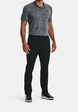 Man wearing a gray patterned polo shirt, black pants, black belt, and black athletic shoes, standing against a plain background.