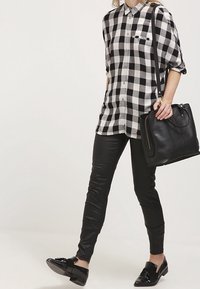 Ruudullinen mustavalkoinen paita nappimallisella tyylillä, yhdistettynä tiukkoihin mustiin nahkahousuihin ja kiiltäviin mustiin kenkiin. Mustaa käsilaukkua pidetään kädessä.