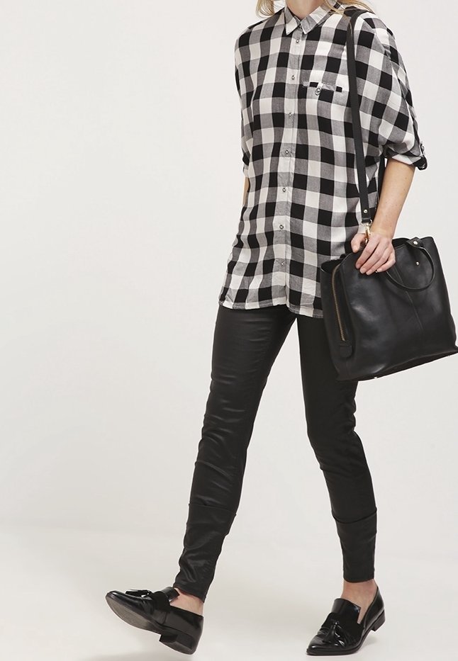 Ruudullinen mustavalkoinen paita nappimallisella tyylillä, yhdistettynä tiukkoihin mustiin nahkahousuihin ja kiiltäviin mustiin kenkiin. Mustaa käsilaukkua pidetään kädessä.