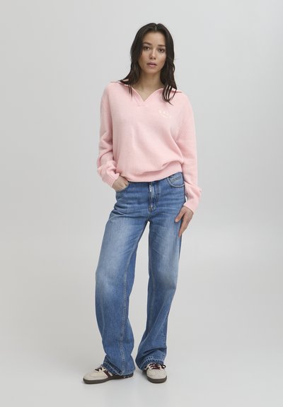 Roza pletena džemper s V-izrezom i rebrastim rukavima, uparen s svijetloplavim širokim trapericama i bežtenisicama s bordos detaljima.