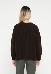 Brun strikket genser med en løs passform, med rund hals og ribbestrikkede mansjetter. Teksturen ser myk og fluffy ut, egnet for hverdagsbruk.