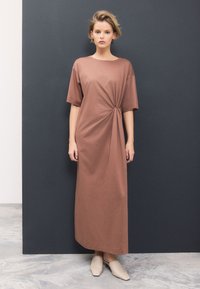 Brun klänning till knäna med lös passform, korta ärmar, detalj med sidoknut och slät textur. Kombinerad med ljusfärgade slip-in skor.