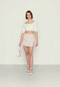 Top branco com ombros à vista e mangas balão, com acabamento em renda, combinado com uma saia mini rosa clara com um padrão subtil, e uma bolsa a condizer.