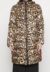 Abrigo acolchado de estampado de leopardo con un acabado brillante y acolchado. Presenta un cierre con cremallera en la parte delantera y una capucha. Bolsillos laterales y acentos multicolores en los laterales.