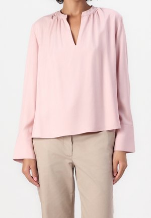 Lyserød langærmet top med en samling ved halsen, v-formet åbning og afslappet pasform. Glat stof med få syninger, kombineret med beige bukser.