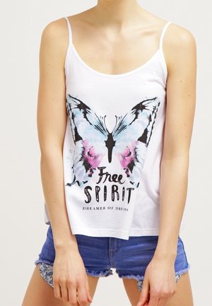 Kvinde iført hvid tanktop med stort blåt og pink sommerfuglemotiv og teksten "Free Spirit Dreamer of Dreams", parret med blå denimshorts.