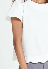 Top bianco a maniche corte con scollo rotondo e orlo scallop, realizzato in tessuto morbido, con vestibilità ampia e dettagli di design minimi.