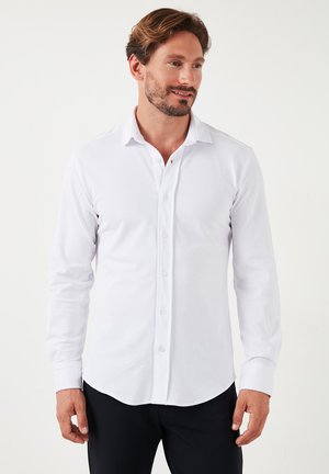 Camisa blanca de manga larga con cuello puntiagudo, cierre frontal de botones y una tela suave y elástica para mayor comodidad.