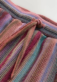 Gros plan d’un tissu tricoté multicolore avec des rayures horizontales en rose, violet, bleu sarcelle et or, noué en un nœud sur le bord supérieur.