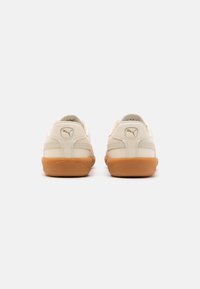 Zapatillas de cuero beige con suela de goma, forma redondeada y logotipo de Puma en el talón. Detalles texturizados en los laterales.