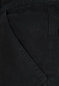 Material negru cu o textură netedă, având o buzunar lateral și cusături subtile de-a lungul cusăturii. Design compact și ajustat.