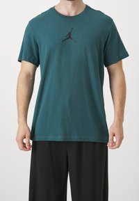 Teal bomulls t-shirt med rundad hals och korta ärmar. Har en svart Jordan-logotyp tryckt på bröstet. Matchas med svarta byxor.