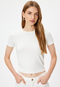Hvid, kortærmet bomulds t-shirt med rund halsudskæring og cropped design, båret med hvide denim bukser. Glat tekstur.
