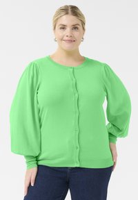 Lys grøn cardigan med rund hals, knaplukning og puffede lange ærmer. Lavet af blødt materiale med ribbede manchetter og kant.