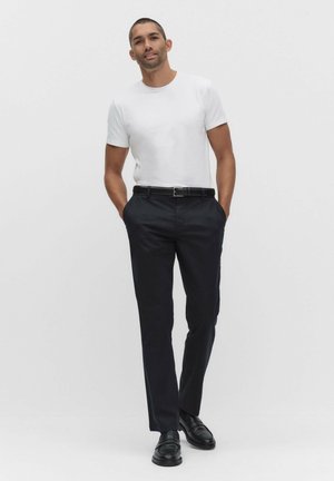 Vit t-shirt med korta ärmar kombinerad med mörkblå klänningsbyxor och svarta skor. Outfiten har en enkel design och skräddarsydd passform.