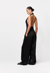Fekete pánt nélküli body nyitott háttal, széles szárú fekete szatén nadrággal párosítva. Simogató textúra és minimalista dizájn.