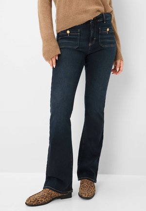 Donkerblauwe flared jeans met een soepele textuur, voorzien van voor- en achterzakken en hardware in goudkleur. Gemaakt met een paar laarzen met luipaardprint.