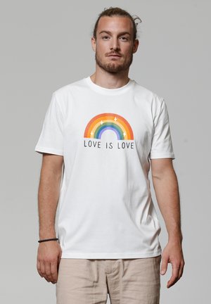 Witte katoenen t-shirt met een meerkleurige regenbooggrafiek en de tekst "LIEFDE IS LIEFDE" gecentreerd eronder, korte mouwen en ronde hals.