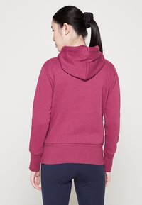Bordeauxfarbener Kapuzenpullover mit großer Kapuze, aus weichem Stoff gefertigt. Mit gerippten Bündchen und Saum. Getragen mit navyfarbenen Leggings.