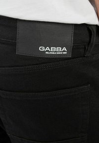 Svarta denimjeans med en slät yta, med en bakficka märkt "GABBA" och accentstygn på fickorna.