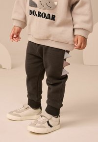 I pantaloni della tuta grigio scuro presentano punte testurizzate in tonalità di rosa e grigio sui lati, abbinati a una felpa beige chiaro e sneakers beige.