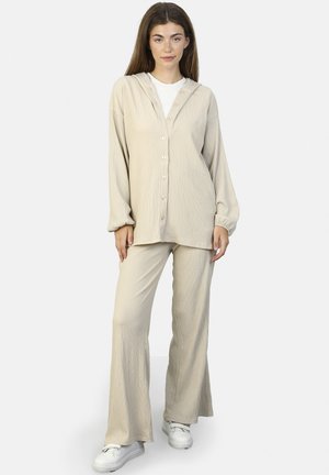 Beige, textured loungewear set featuring a hooded, button-up top with long sleeves and matching flared pants. Worn with white sneakers.
