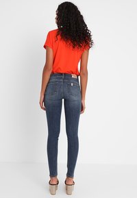 Jeans pitillo azul oscuro de tiro alto, con bolsillos traseros y efecto lavado claro, combinados con una camiseta de manga corta de color naranja brillante.