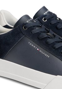 Tenisi navy și albi Tommy Hilfiger cu accente de piele întoarsă, șireturi navy și logo-ul brandului pe lateral și pe limba încălțărilor.
