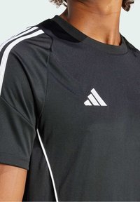 Camiseta deportiva negra con cuello redondo, con rayas blancas a lo largo de los hombros y un logo blanco en el pecho, hecha de tela lisa.